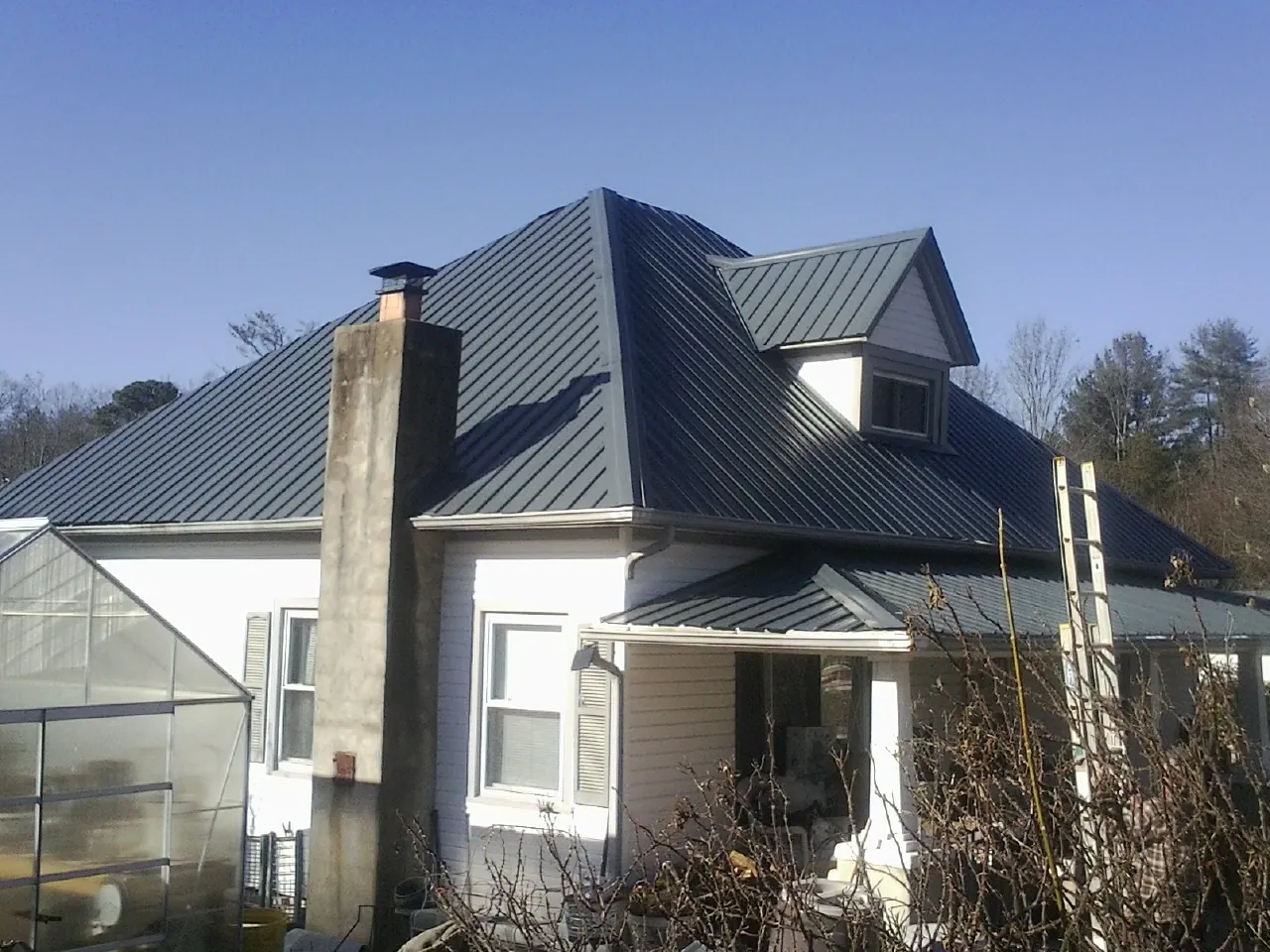Dark blue standing seam metal roof on a white farmhouse with dormer — Slate & Tile Roof Repair by Roofing Brothers in Cordova