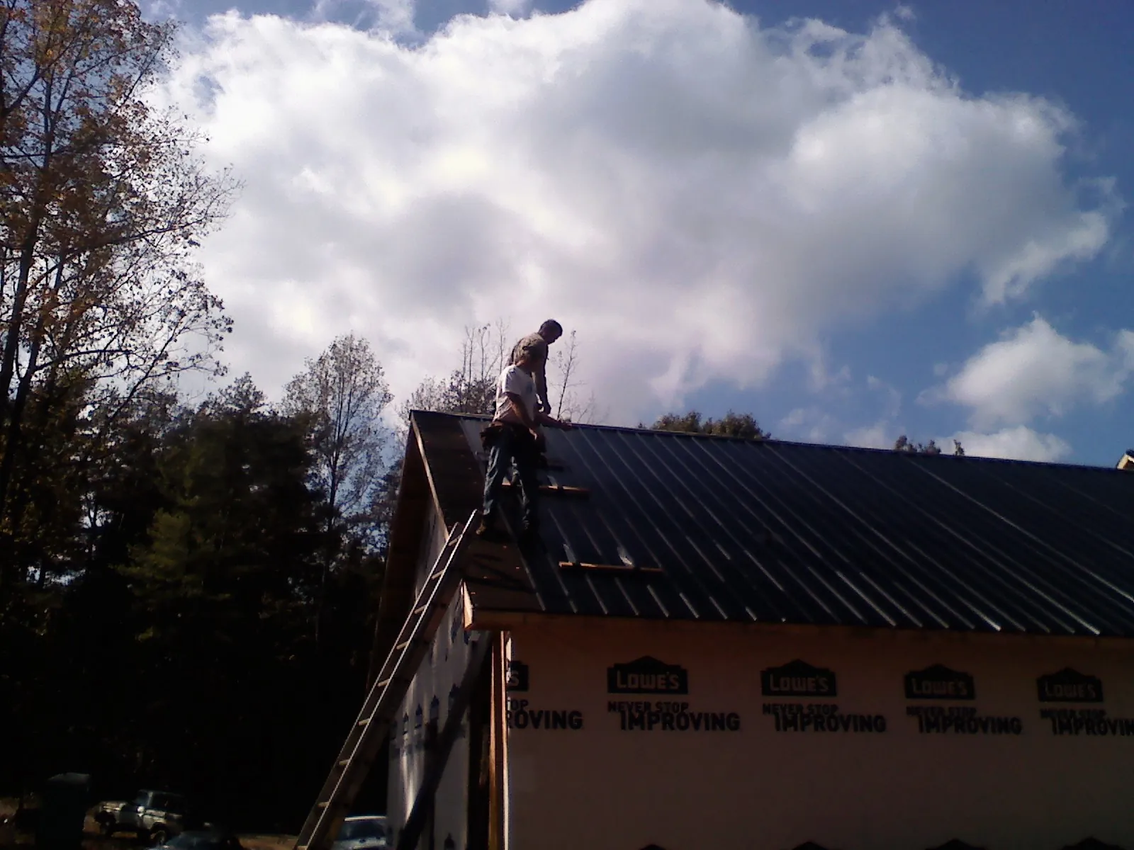 Roofer fastening dark metal panels high against a cloudy sky, from a Roof Inspection job in Cordova
