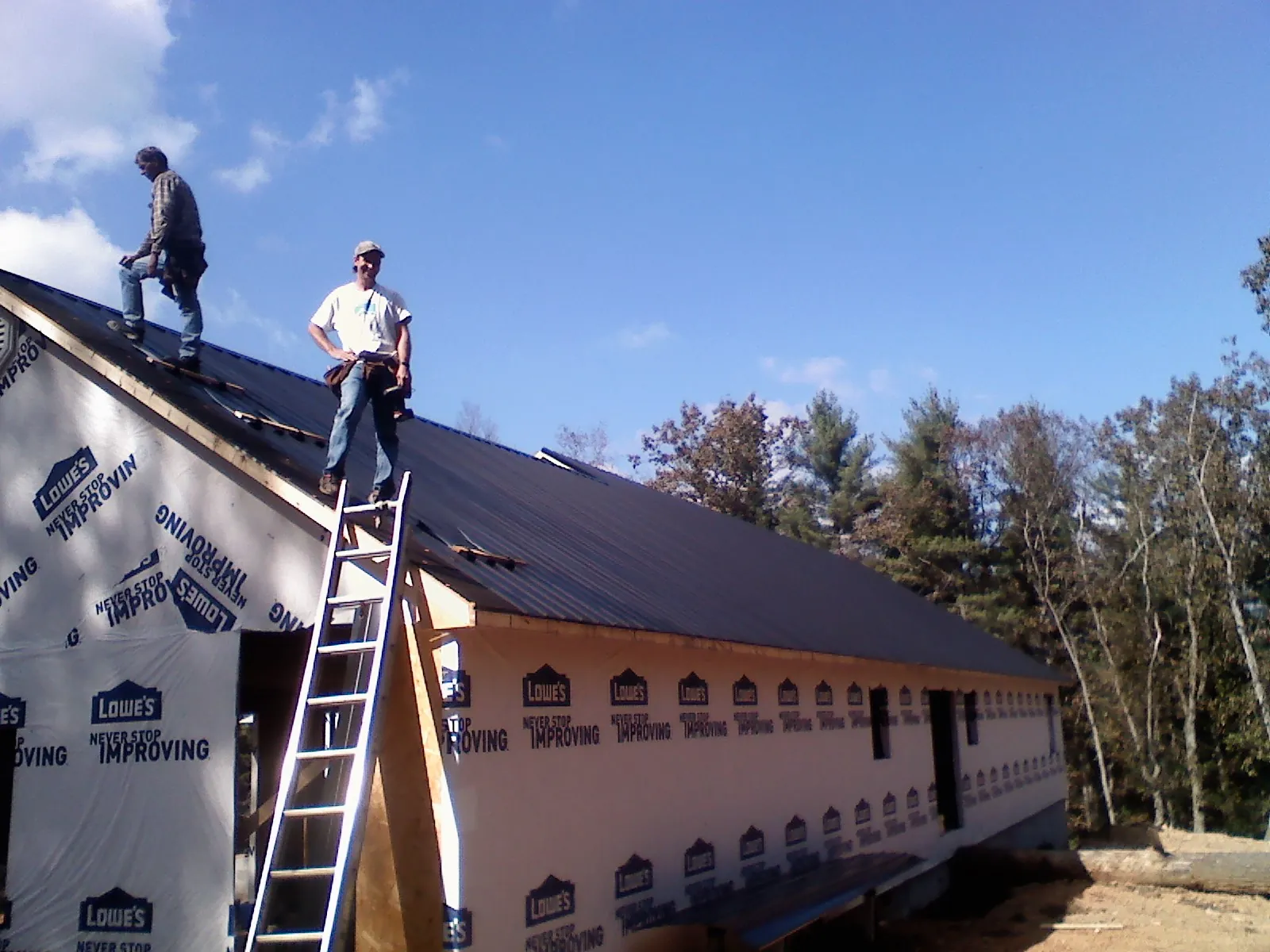 Two roofers standing on a long dark metal roof over a wrapped building in Cordova
